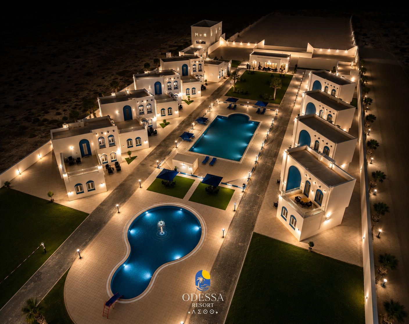 Aerial night view of Odessa Resort with two illuminated pools and whitewashed villas